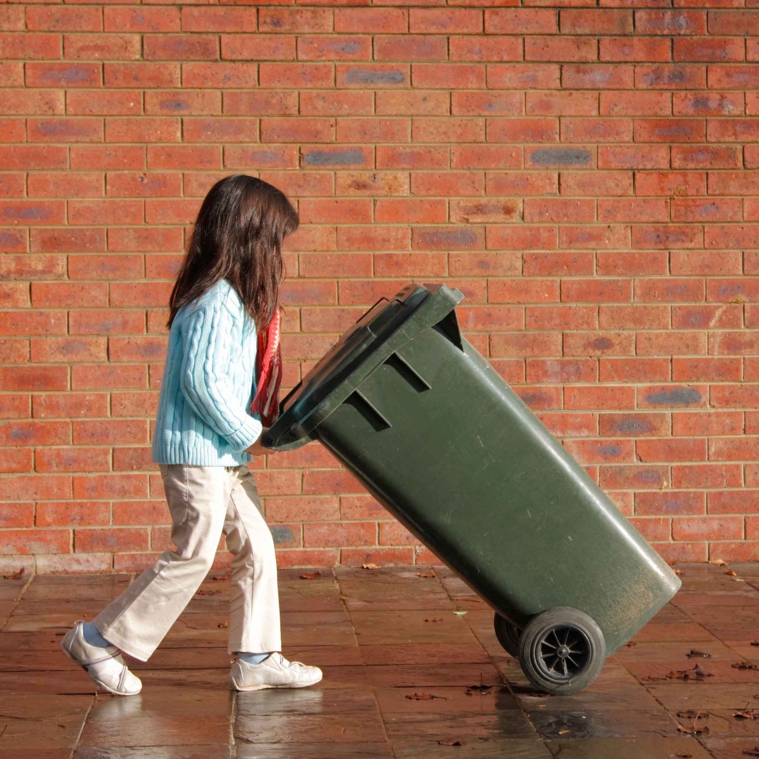 Child pushing a green trash bin against a brick wall got a chore chart for homeschoolers. Ready Set Homeschool