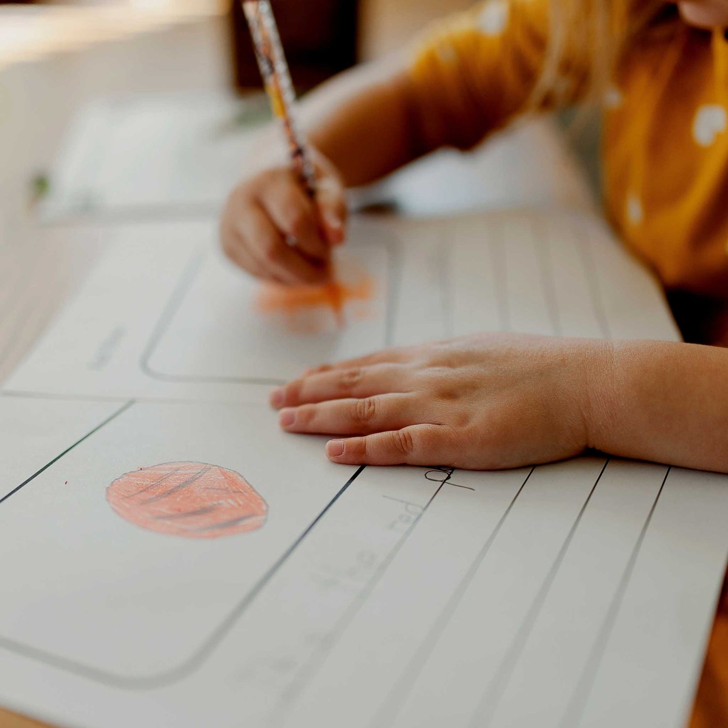 Child's hands coloring on a worksheet with a red crayon. - Ready Set Homeschool